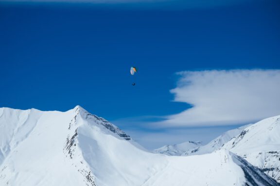 Paraglider flying over Caucasus mountains on a bluebird day.