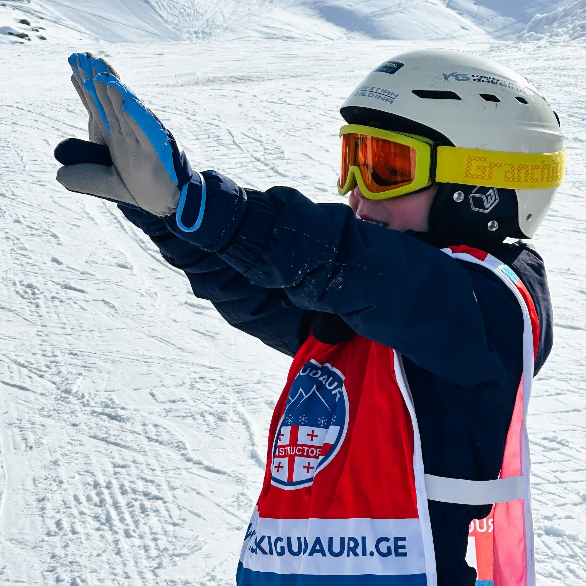 Kid with ski school red bib staying on the ski slope.